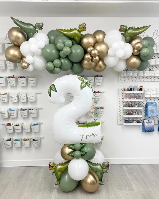 the number two balloon sculpture is decorated with gold, white and green balloons in an office