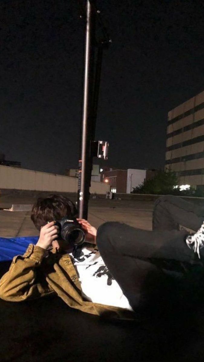 a person sitting on the ground taking a photo with their cell phone at night time