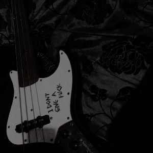 a black and white photo of an electric bass guitar with writing on the body, in front of a floral background