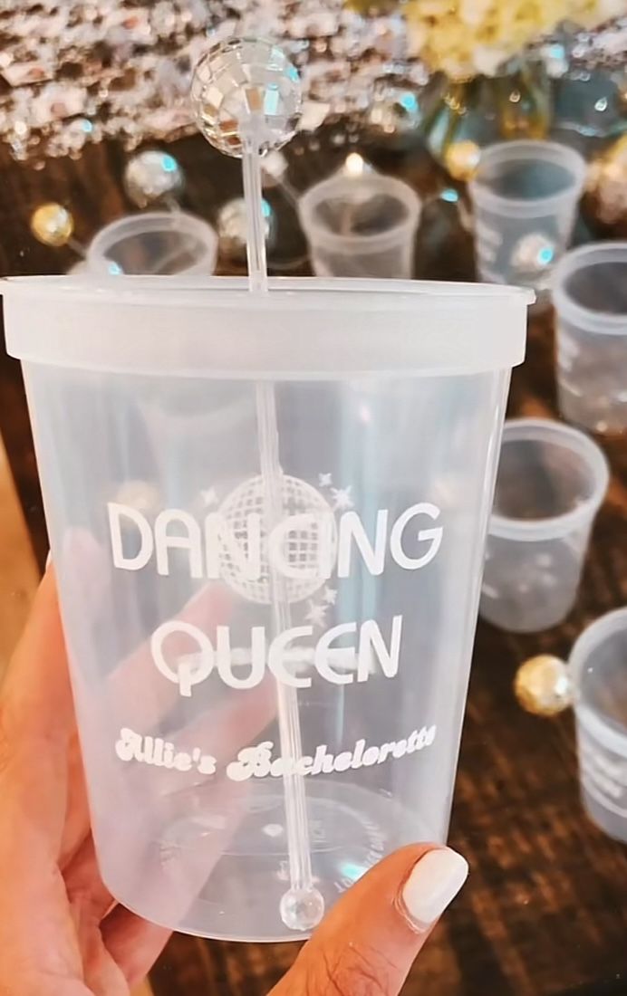 a person holding up a plastic cup with the words dancing queen printed on it in front of other cups