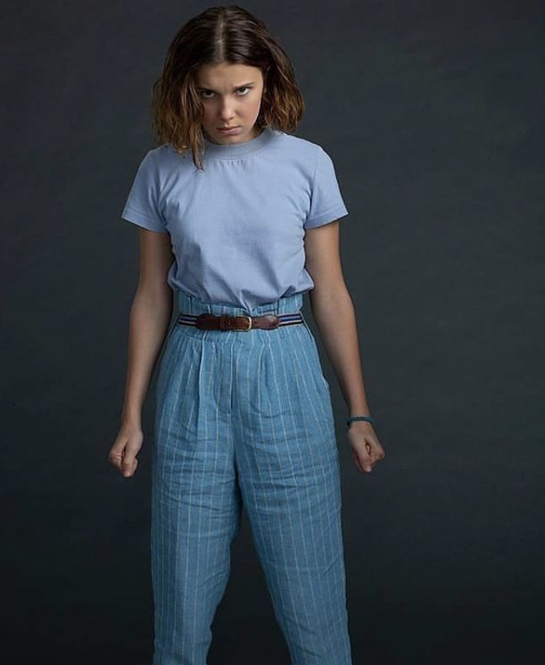 a woman standing in front of a black background wearing blue pants and a t - shirt