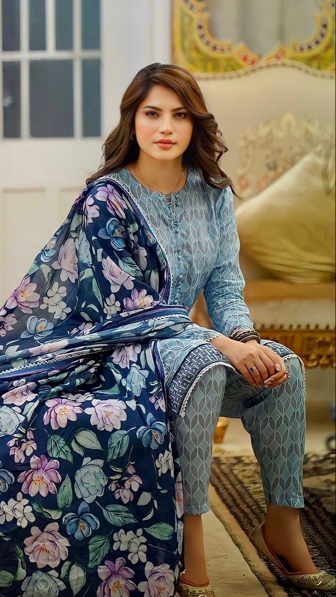 a woman sitting on top of a couch wearing a blue dress and floral print pants