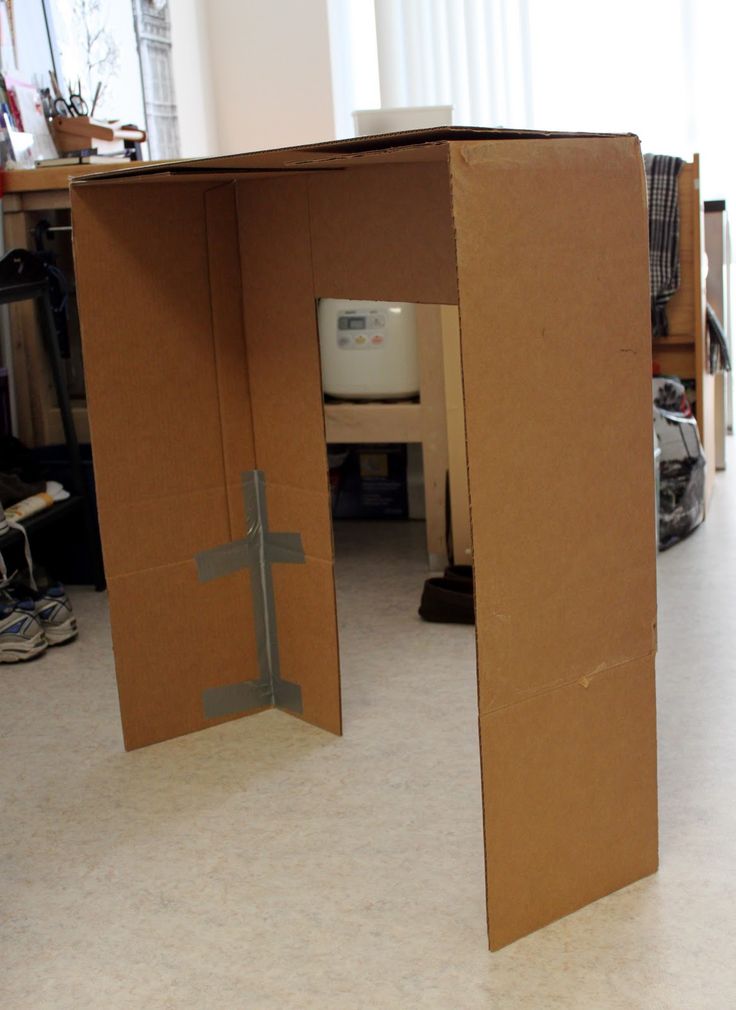 an open cardboard box sitting on the floor in front of a desk with a cross cut out of it