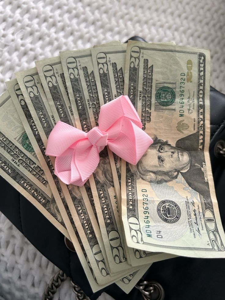 a pink bow sitting on top of money in a purse