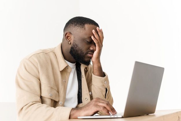 a man sitting at a desk with his head in his hands while looking at a laptop