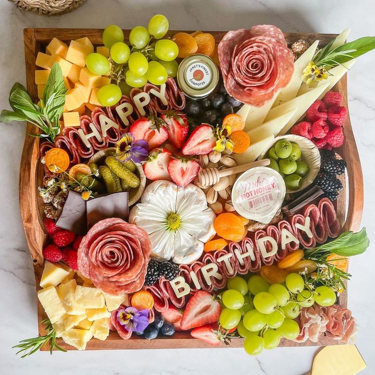 a wooden platter filled with lots of different types of cheeses and fruit on top of a white table