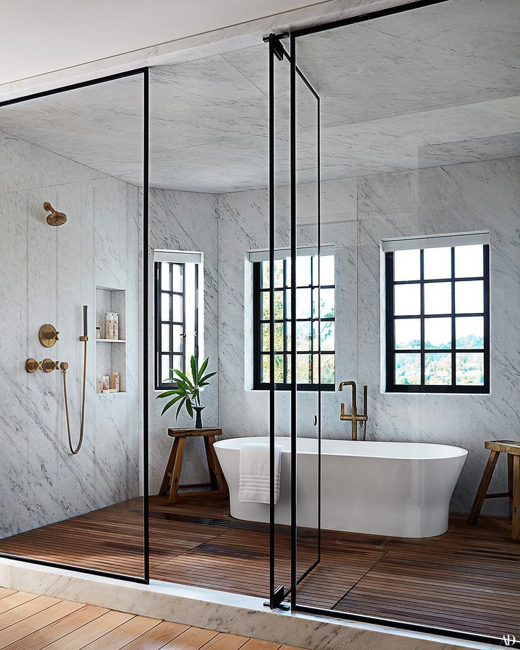 a bathroom with a tub, shower and wooden flooring in front of two windows