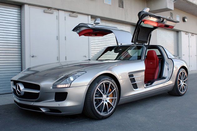 a silver mercedes sls parked in front of a garage with its doors open and the door opened