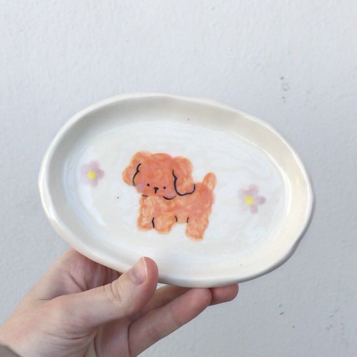 a hand holding a white plate with a small orange dog on it