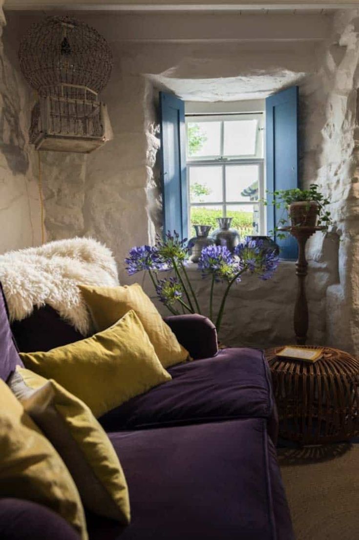 a living room filled with lots of furniture and flowers in front of a window that has blue shutters