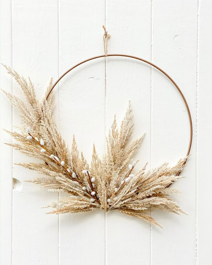 a circular wreath with dried grass hanging from it's side on a white wall