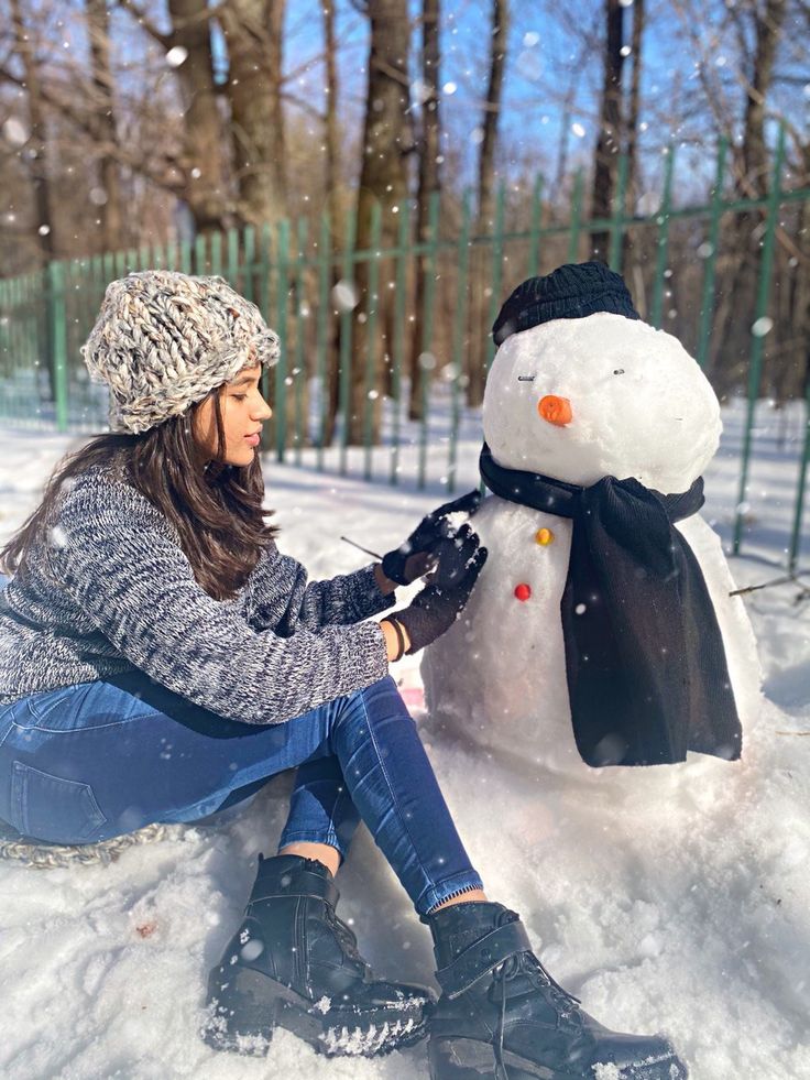 a woman sitting in the snow next to a snowman