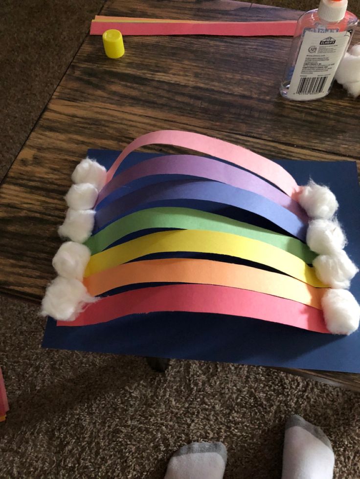 a rainbow craft made out of construction paper and cotton balls on top of a wooden table