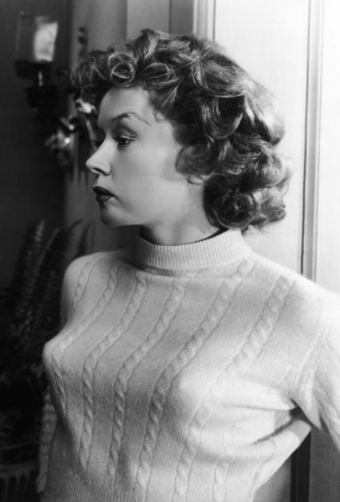 an old black and white photo of a woman in a sweater looking at something on the wall