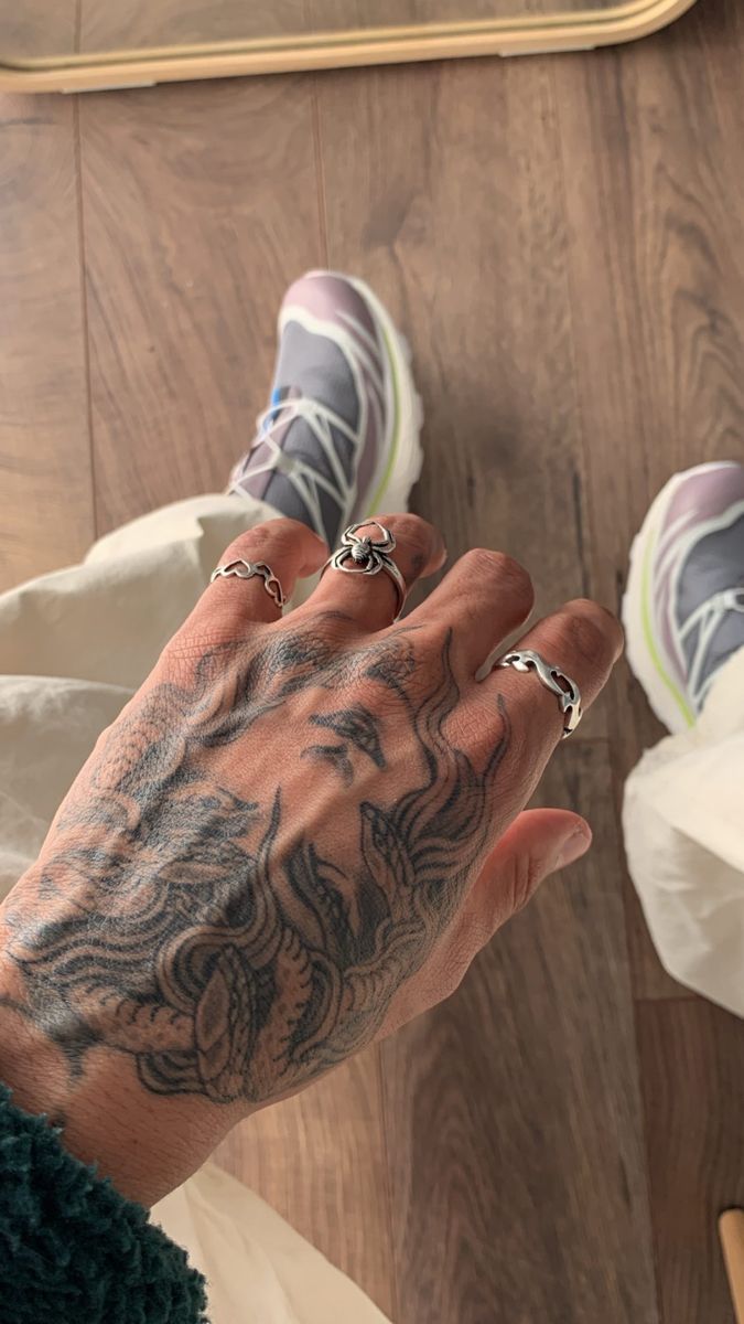 a person's hand with tattoos and rings on it, next to a skateboard