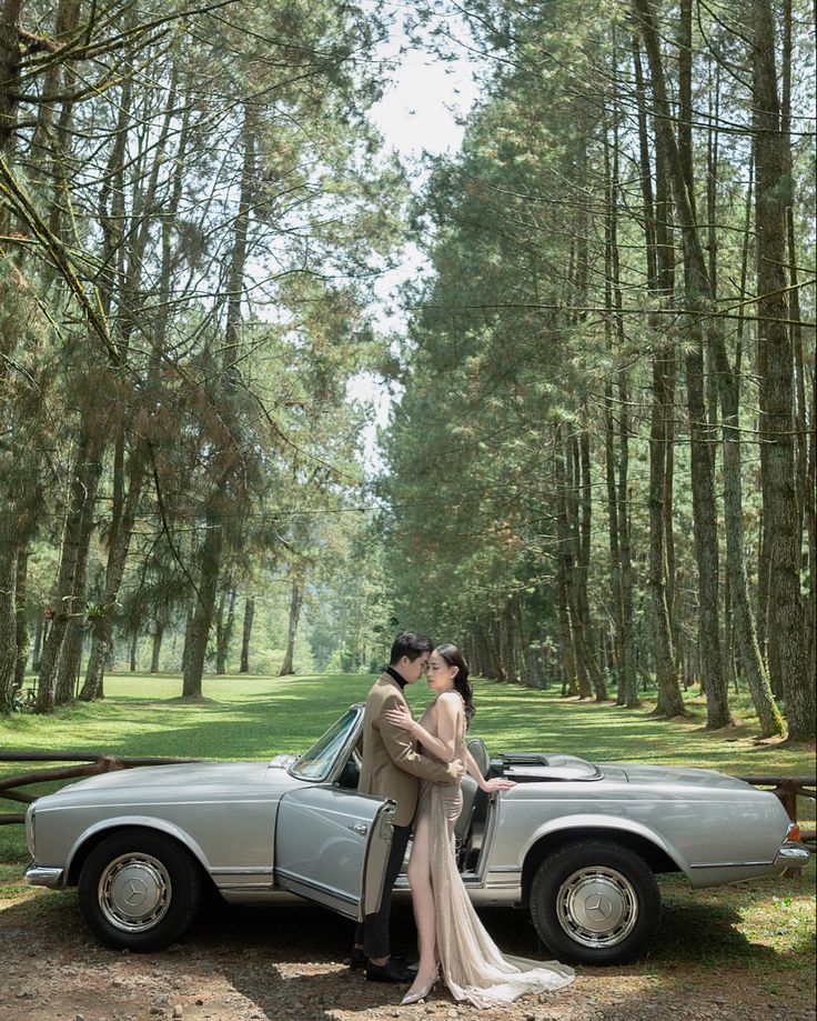 a bride and groom standing in front of a vintage car