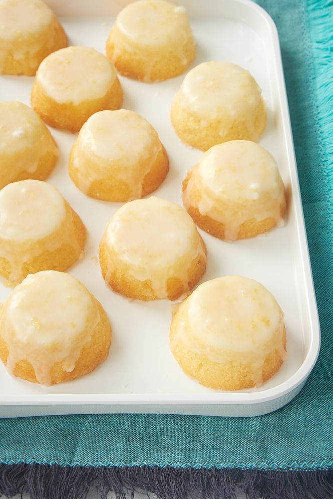 a white tray filled with glazed donuts on top of a blue table cloth next to a cup of coffee