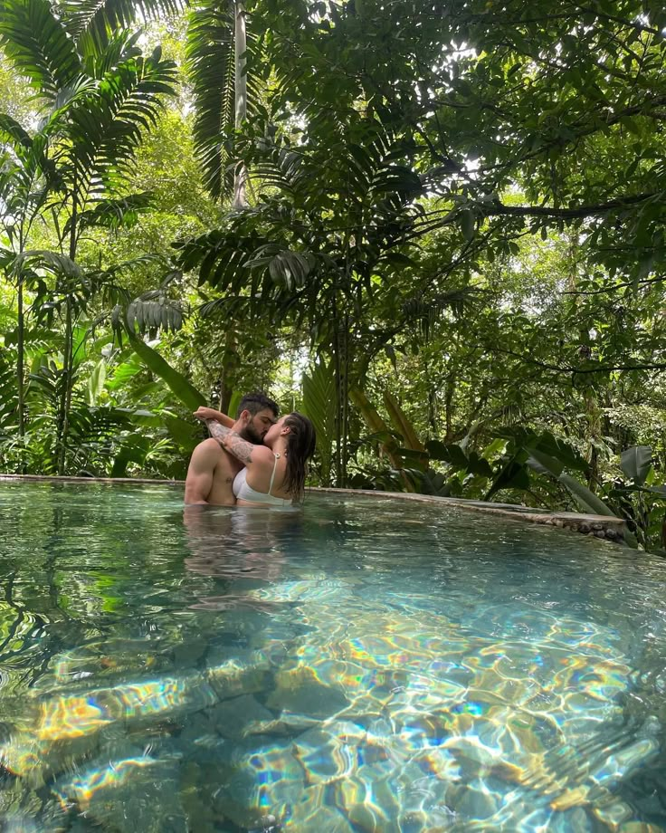 two people sitting in the middle of a swimming pool surrounded by trees and greenery