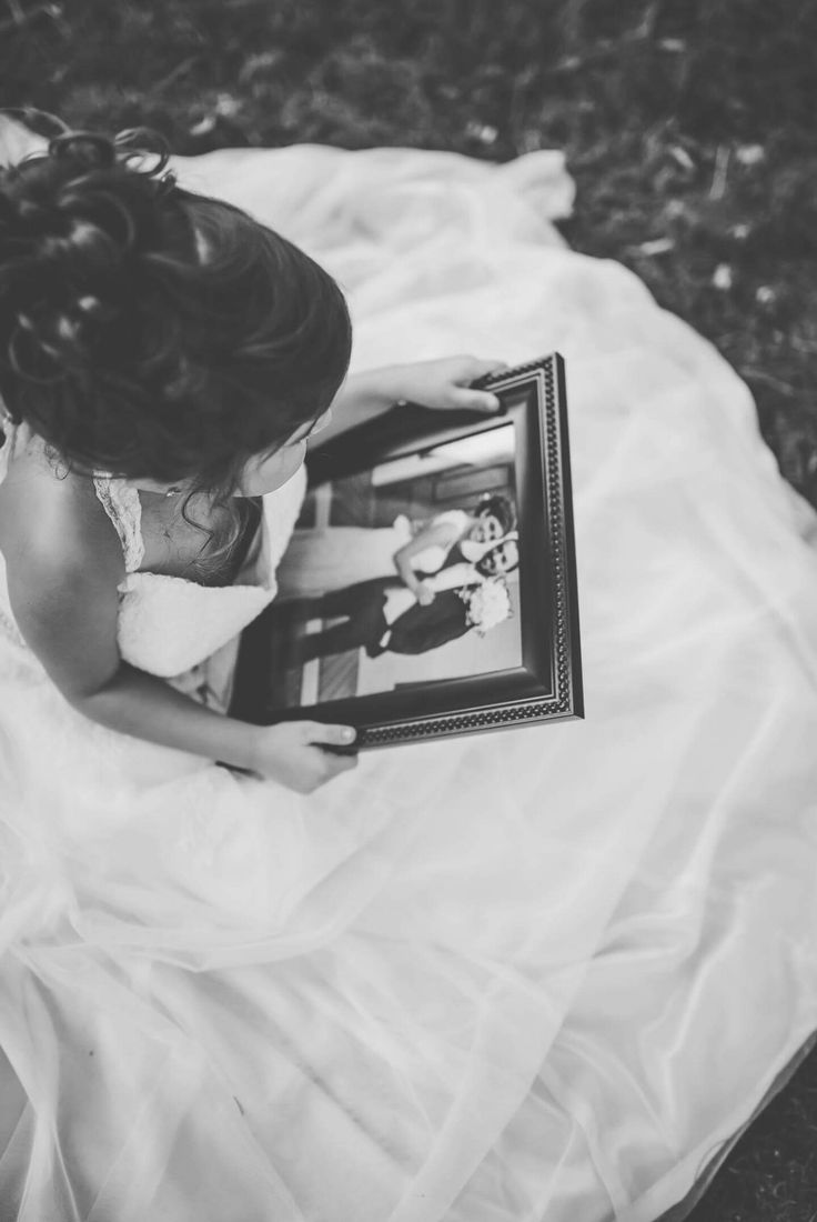 a woman in a wedding dress is holding a framed photo and looking down at it