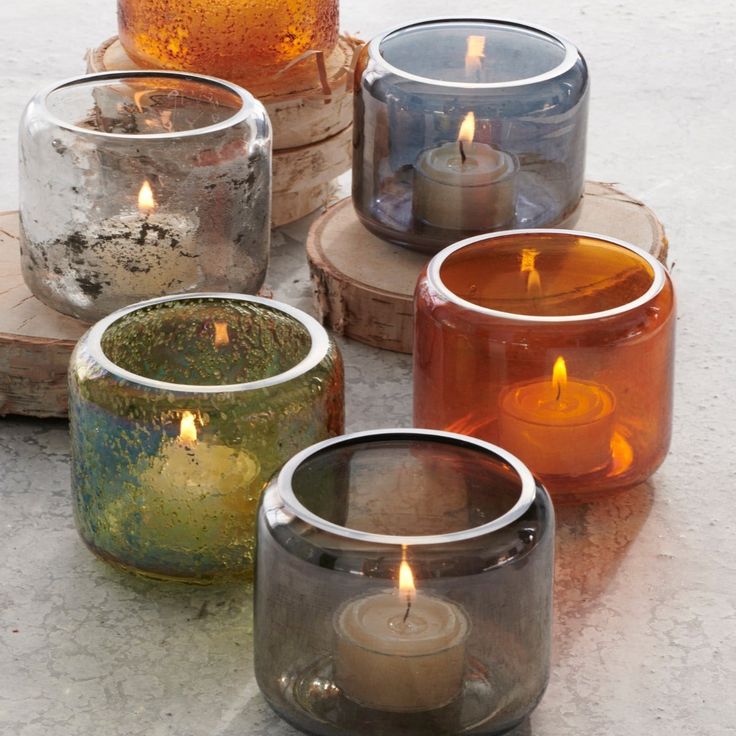 four different colored candles sitting on top of each other in small glass containers with wood slices around them