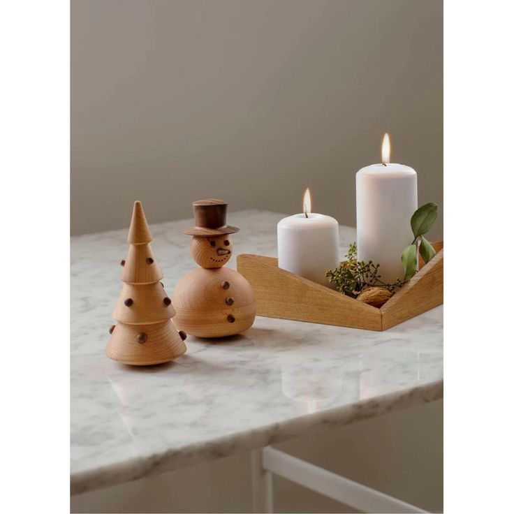 three candles are sitting on a marble counter top next to two small wooden christmas trees