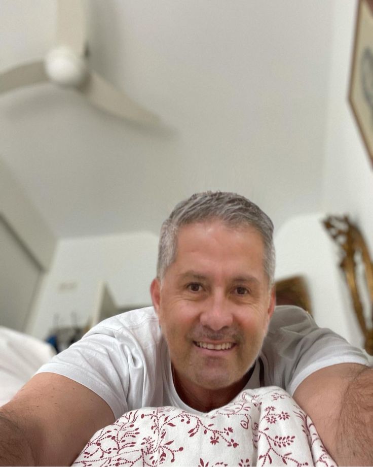 a man laying on top of a bed next to a white wall and ceiling fan