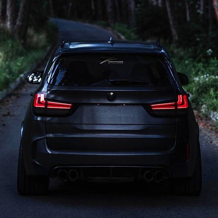 the back end of a black car parked on a road in front of some trees