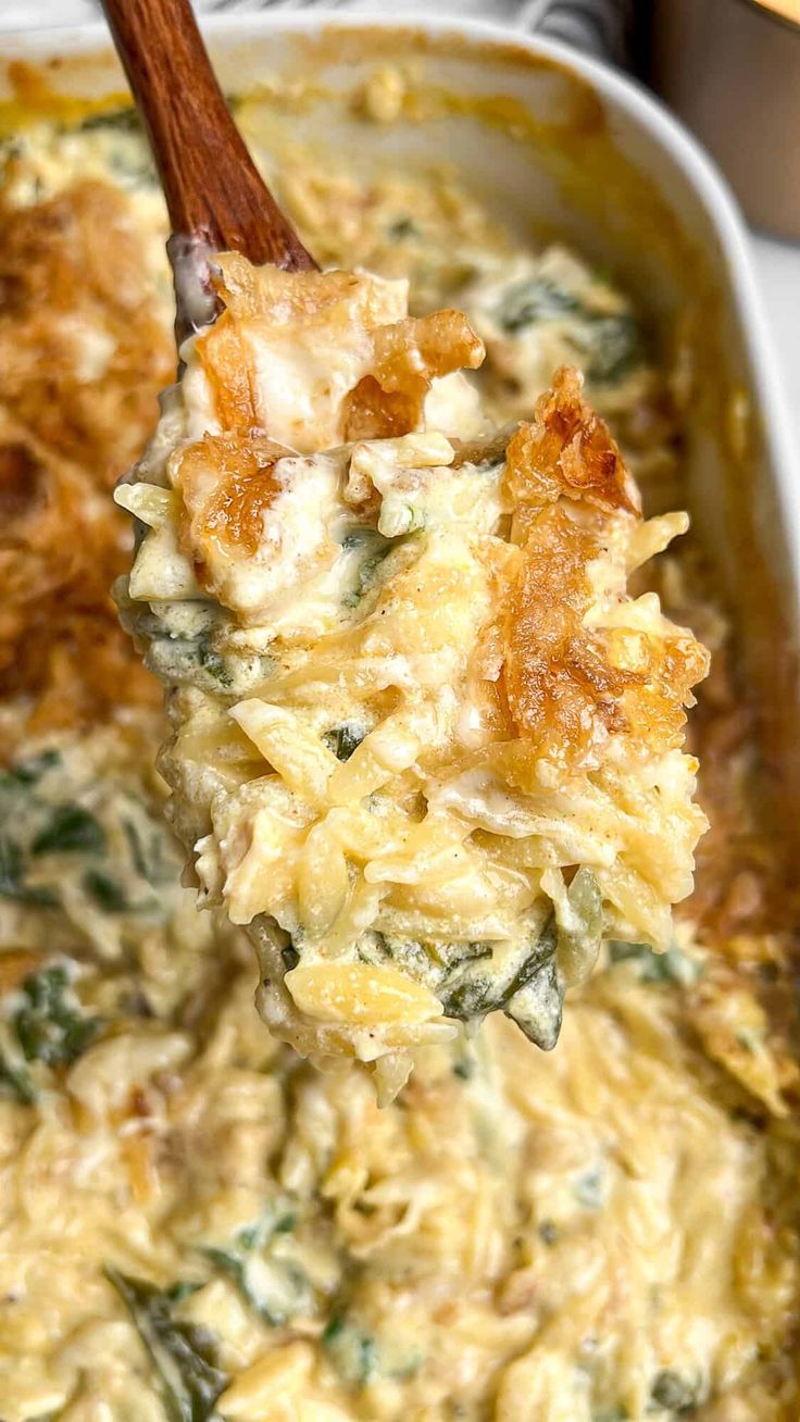 a wooden spoon full of food in a casserole dish with spinach and cheese