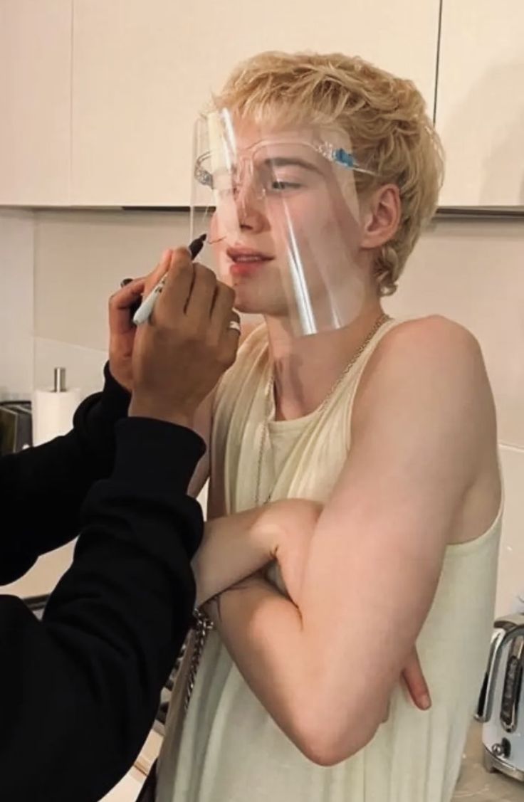 a man getting his nose taped by another person in the kitchen with an oxygen mask on