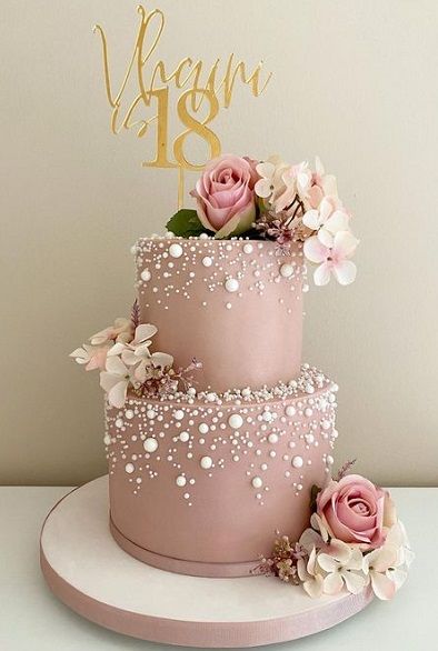 a three tiered cake with pink flowers on top and a gold sign that says vegan