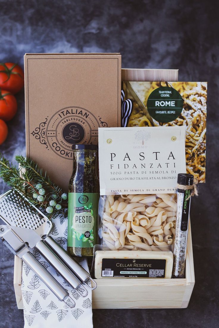 an assortment of italian food and cheeses in a wooden box next to some tomatoes