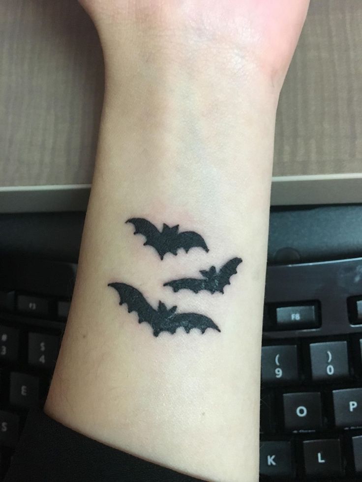 a wrist tattoo with three bats on it and a computer keyboard in the foreground