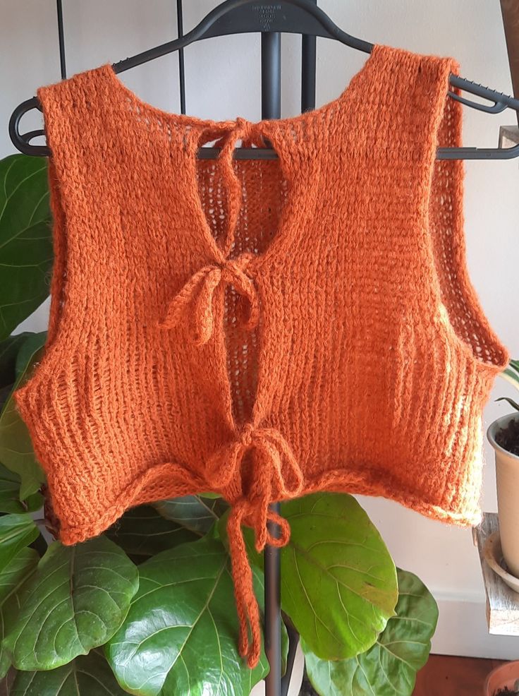 an orange knitted sweater hanging on a rack next to a potted green plant