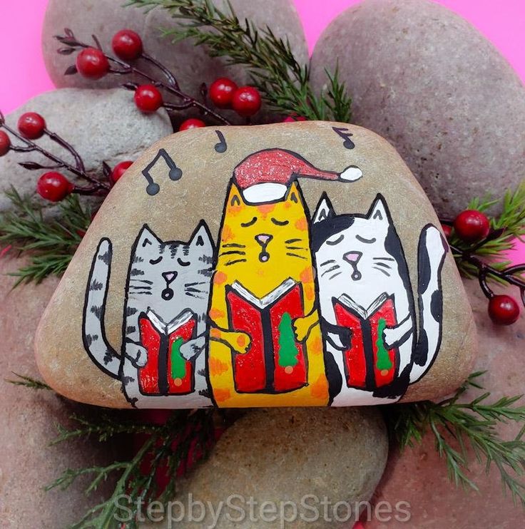 a rock with cats painted on it sitting in front of some rocks and evergreen branches