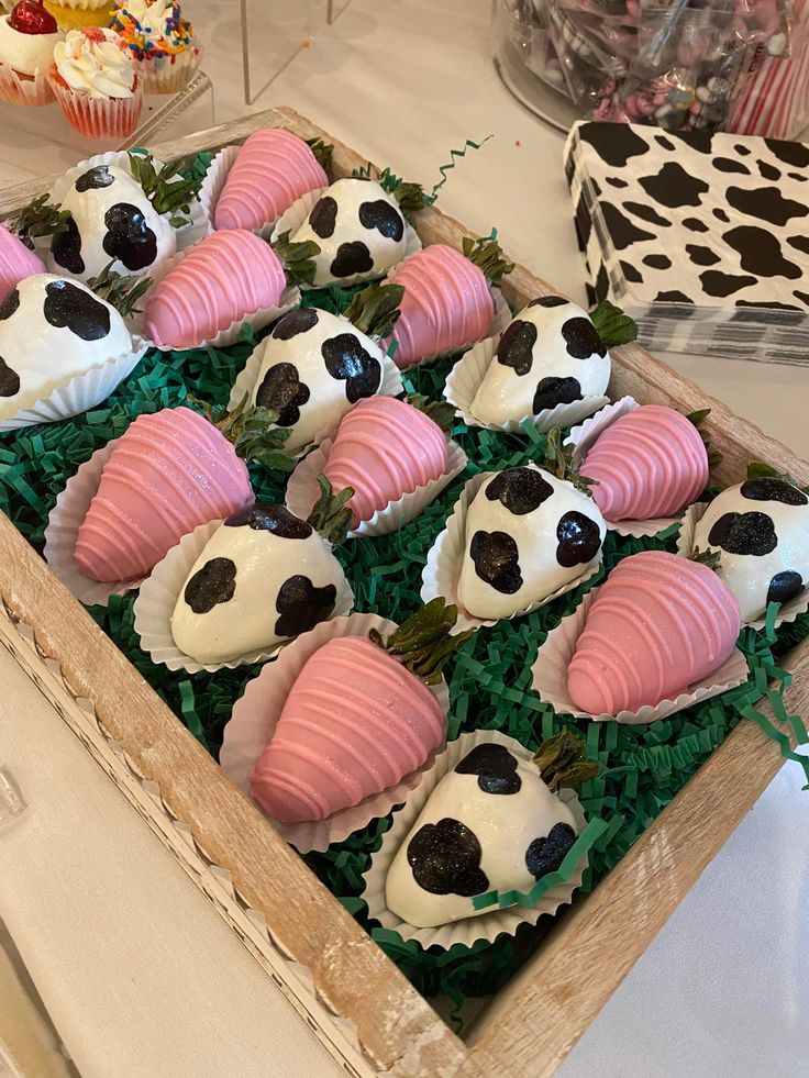 there are many cupcakes in the box on the table with pink and white frosting