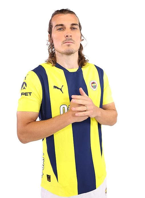 a man with long hair wearing a yellow and blue striped shirt standing in front of a white background