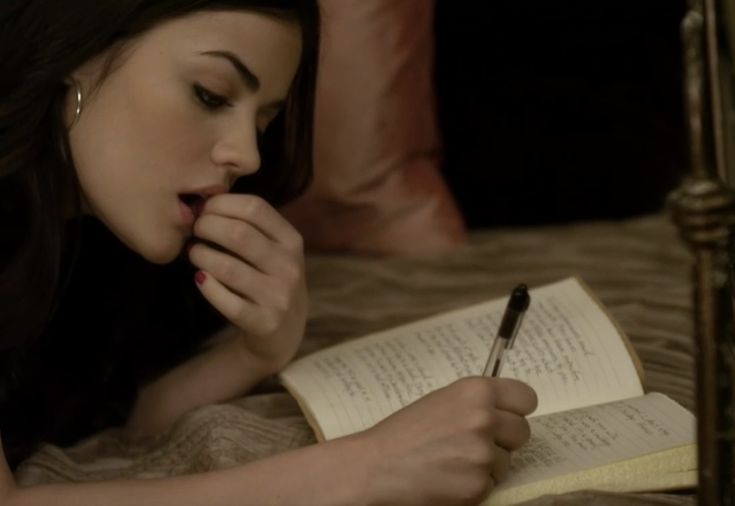 a woman laying in bed reading a book and writing