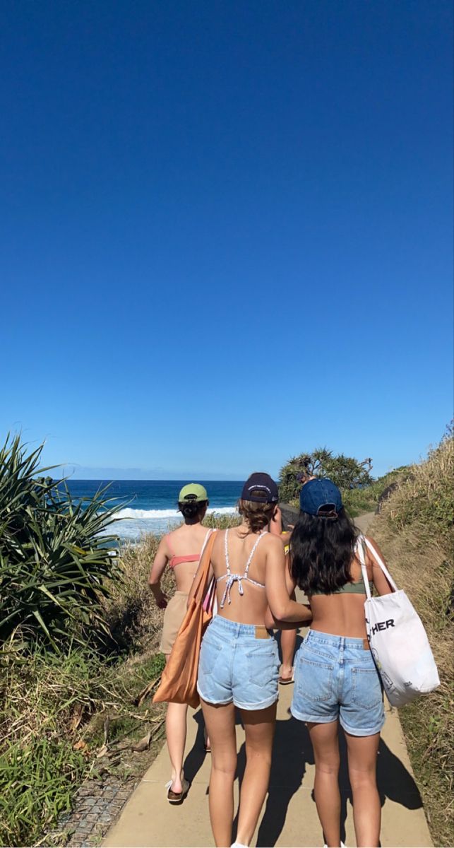 three women walking down a path towards the ocean with their backs to the camera,