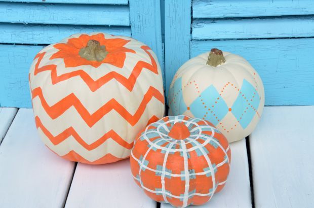 three painted pumpkins sitting next to each other on a white wooden floor in front of a blue door