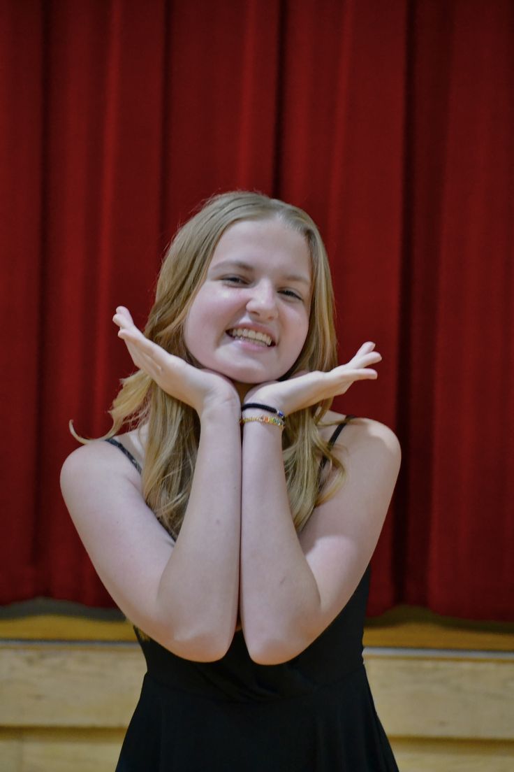 a girl in a black dress is posing with her hands on her chest and smiling