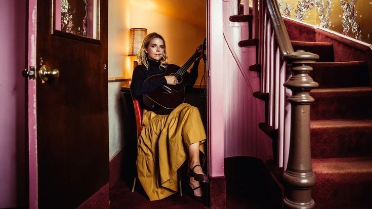 a woman sitting on top of a chair next to a stair case holding a guitar