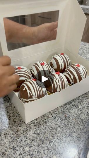 chocolate covered donuts in a white box on a counter top with someone holding one