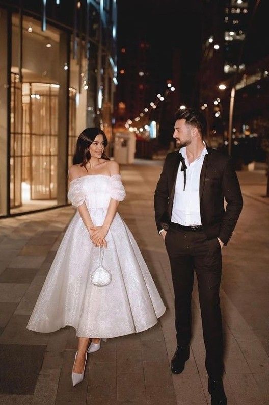 a man and woman in formal wear standing next to each other on a sidewalk at night