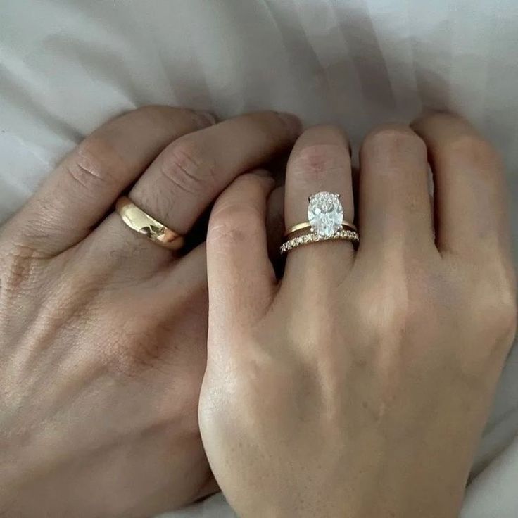 two hands holding each other with wedding rings on top of their fingers and one has a diamond in the middle