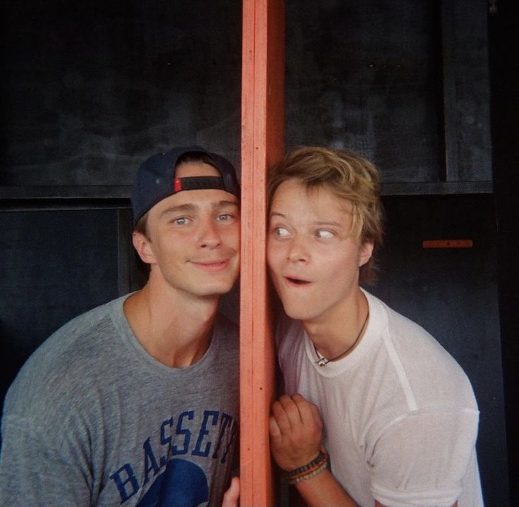 two young men are posing for a photo in front of a tall wooden pole with their eyes closed