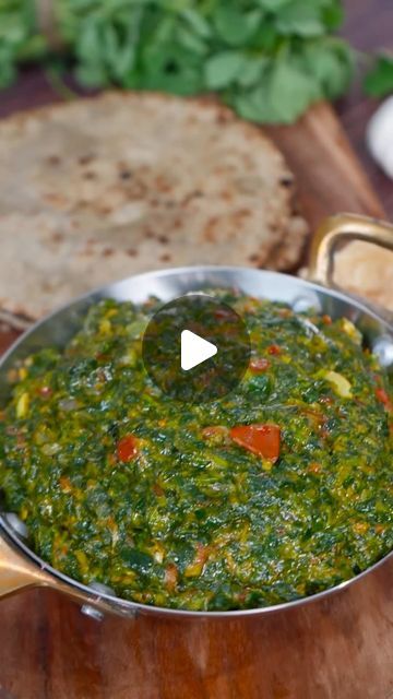 a metal pan filled with green food on top of a wooden table next to pita bread