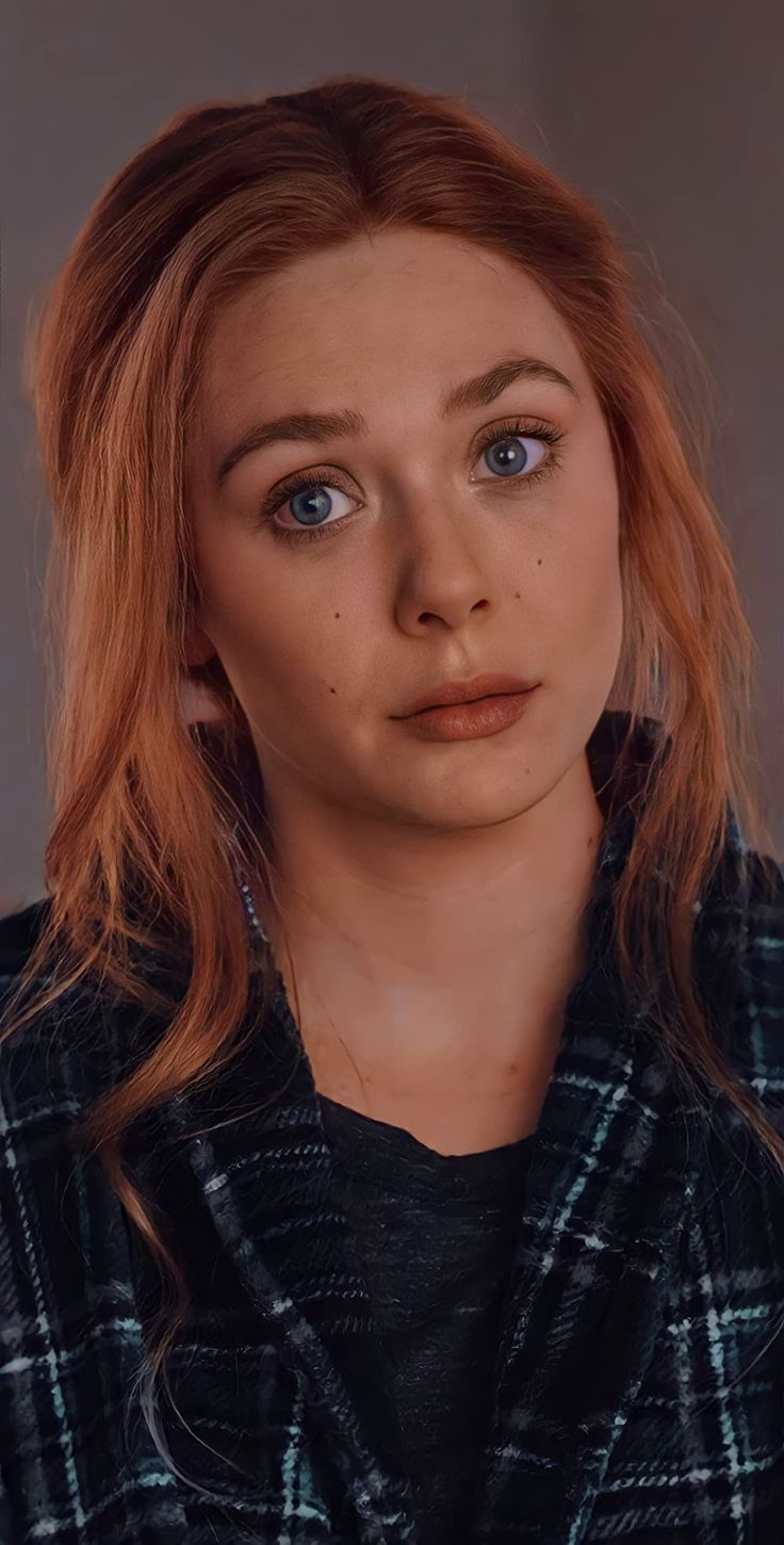 a woman with red hair and blue eyes looks at the camera while wearing a plaid jacket