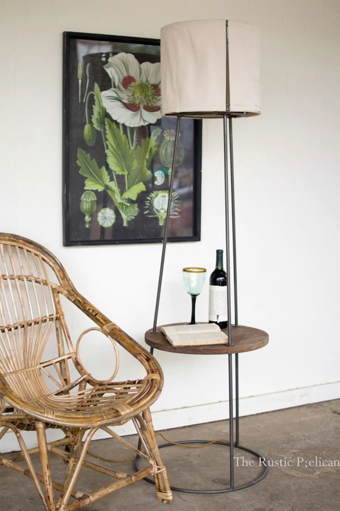 a wicker chair next to a table with a bottle of wine and a painting on the wall