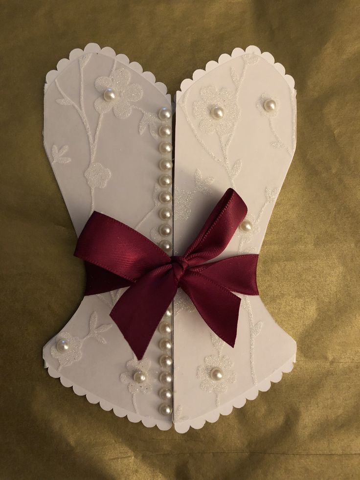 a white card with a red ribbon and pearls on the front is laying on a gold sheet