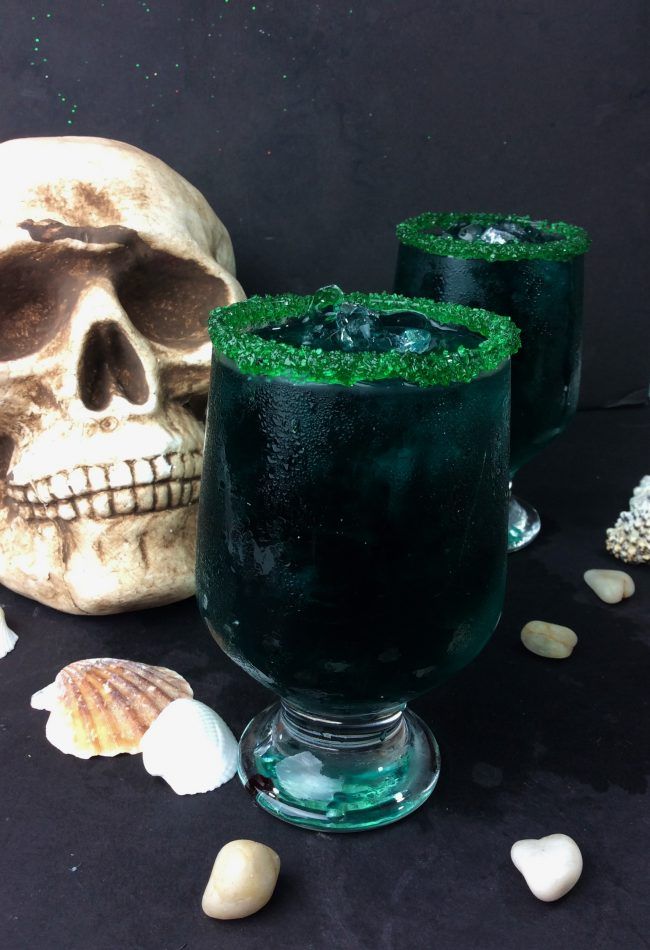 two glasses filled with green liquid next to a skull